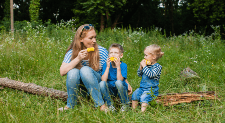 mama și doi copii mâncând porumb fiert în natură