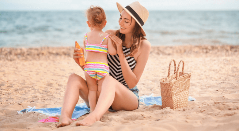 femeie care aplică cremă cu protecția solară pe o fetiță la plajă